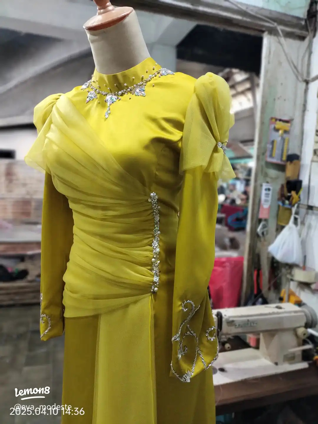 Tampilan samping gaun kuning panjang pada manekin, menunjukkan draperi kain yang elegan dan hiasan payet vertikal di sisi gaun.