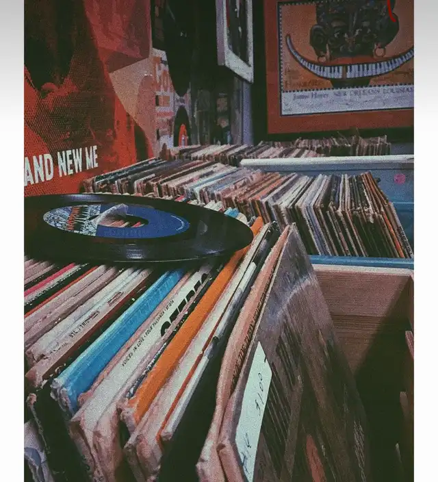 A close-up shot of various vinyl records stacked in a vintage-style setting, with one black record prominently displayed on top. The text 'AND NEW ME' is visible on a red background in the upper left corner.