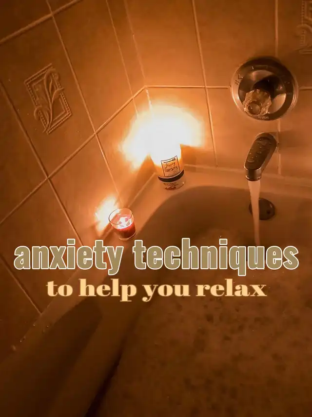A warm, dimly lit bathroom scene with a bathtub filling with water, illuminated by two glowing candles. The image features text about anxiety techniques to help you relax, suggesting a calming self-care routine.
