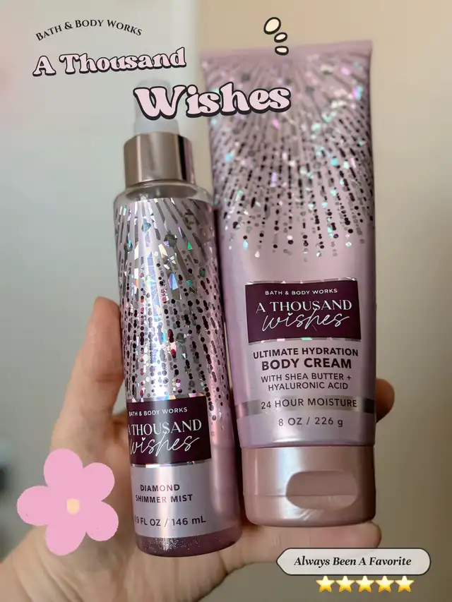 A hand holds a Bath & Body Works A Thousand Wishes Diamond Shimmer Mist and an Ultimate Hydration Body Cream. Both products are pink with shimmering designs, featuring the scent name prominently.