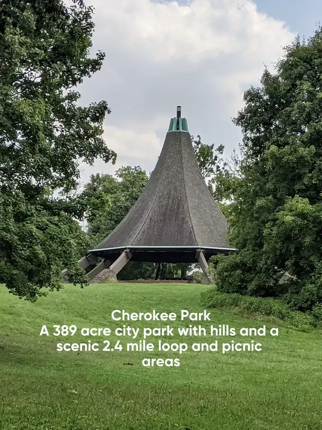 A unique, conical-roofed pavilion stands in a green, grassy field, surrounded by tall trees under a cloudy sky. The image is overlaid with text describing Cherokee Park as a large city park with hills and picnic areas.